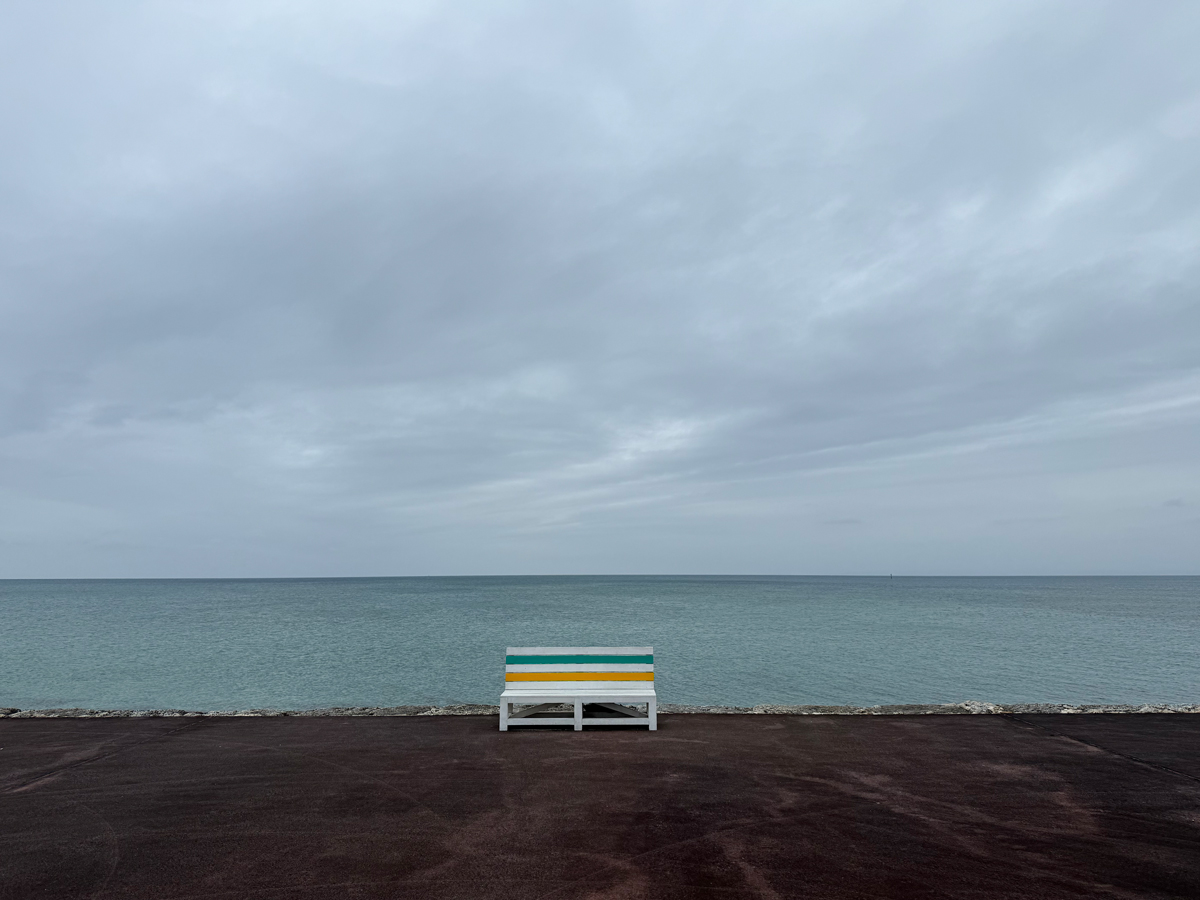 曇った空の下に広がる沖縄の海と、海岸に置かれた白と緑と黄色に塗られたベンチ。
