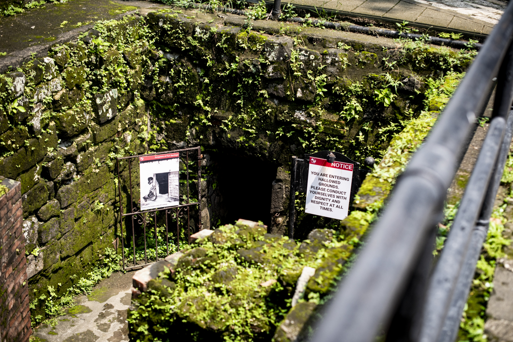 石造りの強固なアーチ状の入り口を持つ、サンチャゴ要塞の地下空間(水牢)の跡地。鉄格子の扉と「NOTICE」と書かれた赤い警告看板が設置されている。