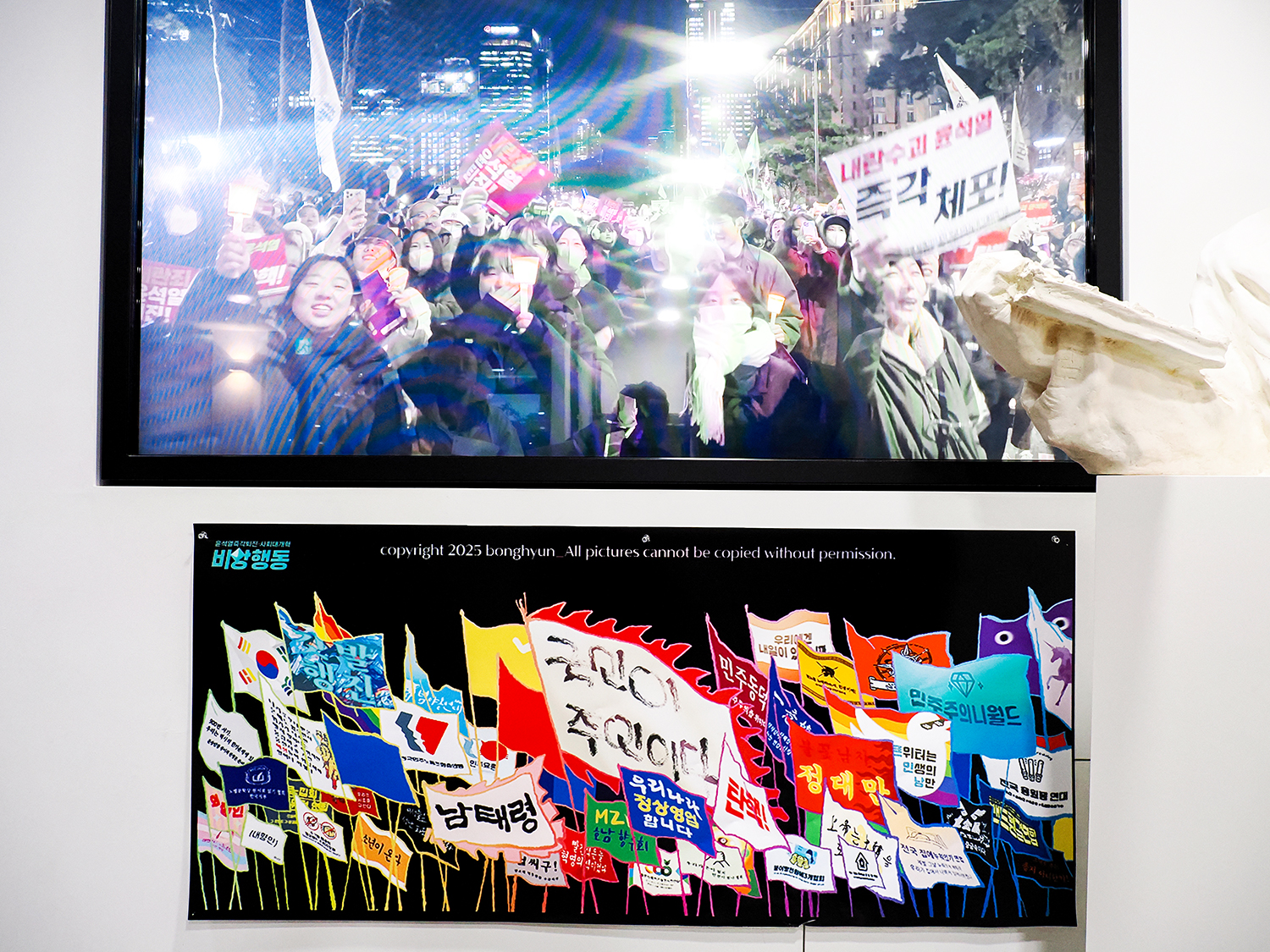 植民地歴史博物館の館内の展示。ここでは、戒厳令を出した尹元大統領に抗議する市民集会の映像と、デモで掲げられた色とりどりな旗を描いた絵が上下に並ぶ。