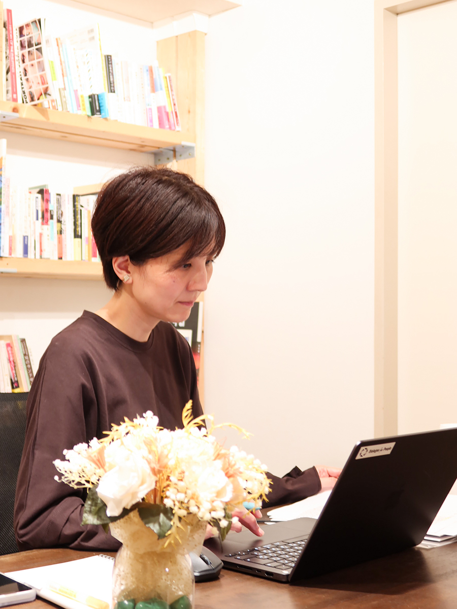 机の上のノートパソコンの前に座るDialogue for Peopleスタッフ・伏見