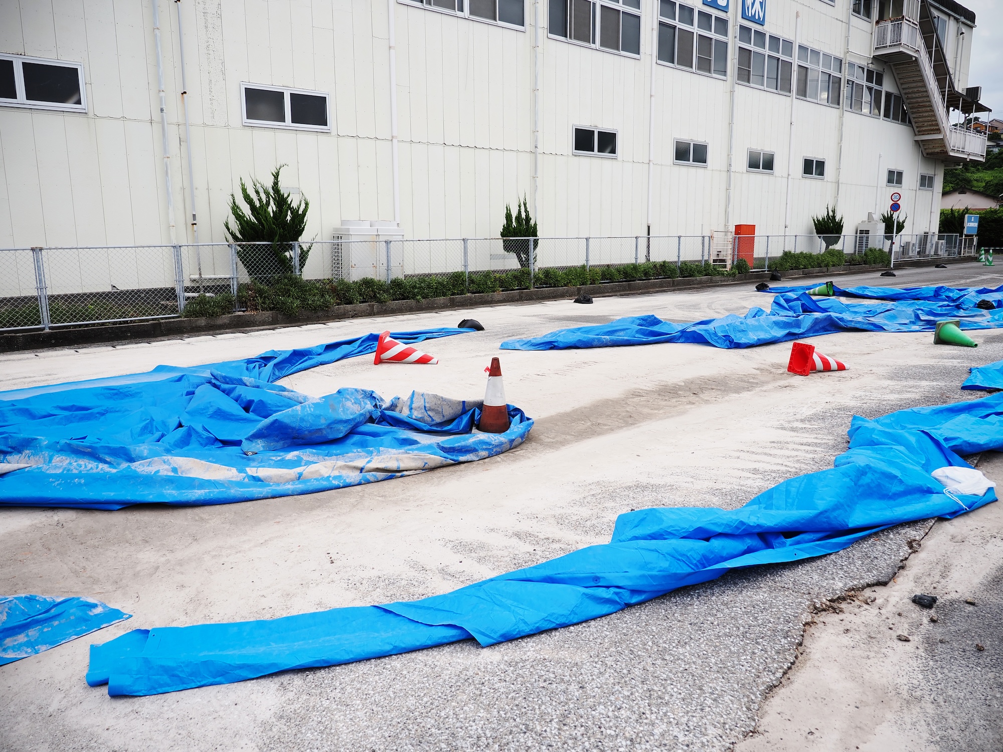 地面に青いシートが敷かれ、三角コーンが点在しているエコパーク水俣隣接の市道